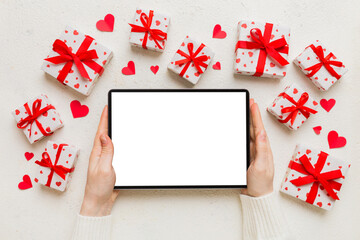 Top view of digital tablet with gift boxes and hearts on colorful background. Tablet with black screen with Holiday decorations gift box top view