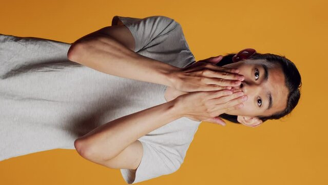 Vertical video: Asian adult sending air kisses on camera, acting funny and romantic in studio. Young carefree person blowing kisses and being flirty, acting sensual with kissy silly face. Natural