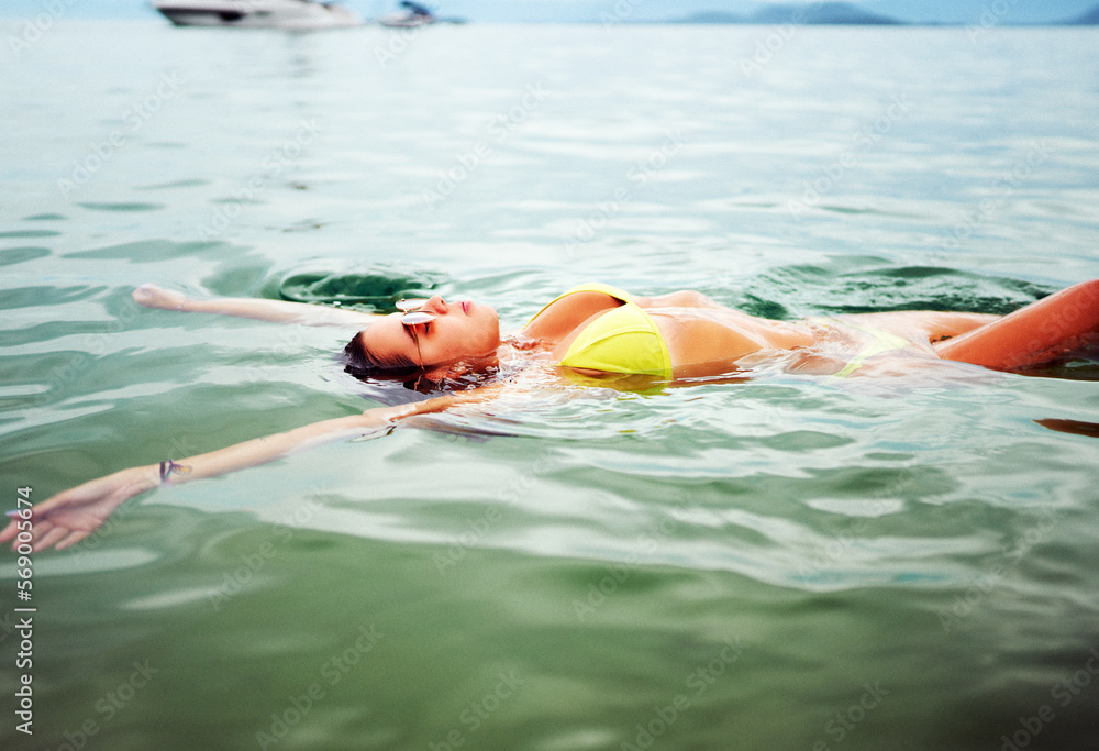 Wall mural young brazilian woman back floating or swimming in the water relaxed with eyes closed enjoying in il