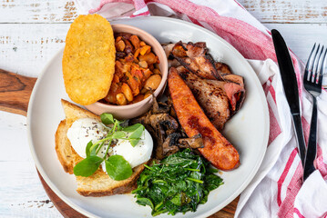 A serving of a country breakfast plate, consisting of bacon, eggs, baked beans, toast, mushrooms, spinach and a hash brown