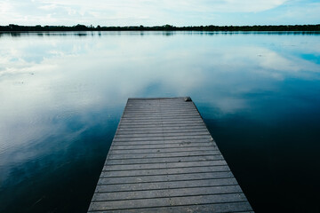 Obraz premium wooden pier on lake reflecting clouds