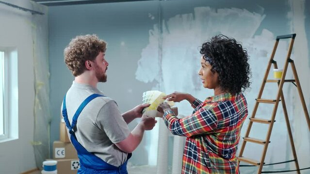 Customer is an African American woman and white male foreman choosing paint color on color palette. Female discussing color of wall painting with master during renovation of apartment, rear view.