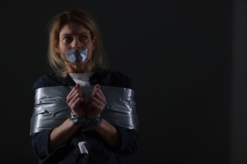 Woman taped up and taken hostage on dark background. Space for text - obrazy, fototapety, plakaty