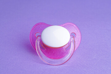 One new baby pacifier on purple background, closeup