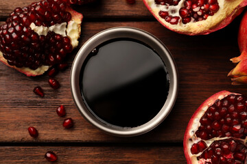 Glass bowl of tasty pomegranate sauce and fresh ripe fruit on wooden table, flat lay