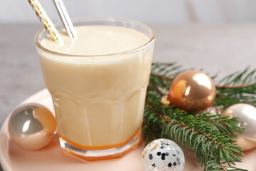 Glass of delicious eggnog and decorated fir branch on gray table, closeup