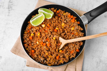 Fried minced meat, carrot, corn and lime in pan on white textured table, top view