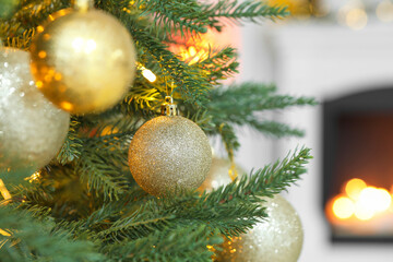 Obraz na płótnie Canvas Beautiful golden Christmas balls hanging on fir tree branch against blurred background, closeup