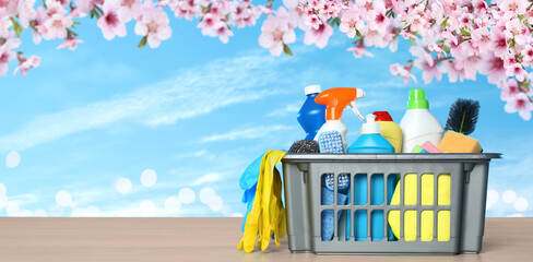 Spring cleaning. Basket with detergents and tools on wooden surface under blossoming tree against...