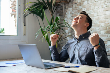 Man sit at desk read e-mail on laptop makes yes gesture feels happy. Male entrepreneur get great...