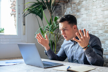 Unhappy young caucasian male worker in glasses look at laptop screen shocked by gadget breakdown or...