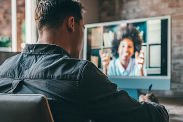 View over shoulder employer listen applicant at job interview online use cam and pc. Young caucasian man with tattoos at home working and talking online with African woman colleague in videocall.