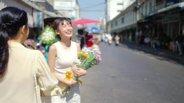 4K Happy Asian family mother and daughter holding flower bouquet and walking together during shopping at florist shop street market for flowers vase arrangement celebrating holiday event at home.