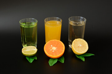 Three glasses with blurred citrus juices on a black background, decorated with leaves and slices of lemon, orange and lime.