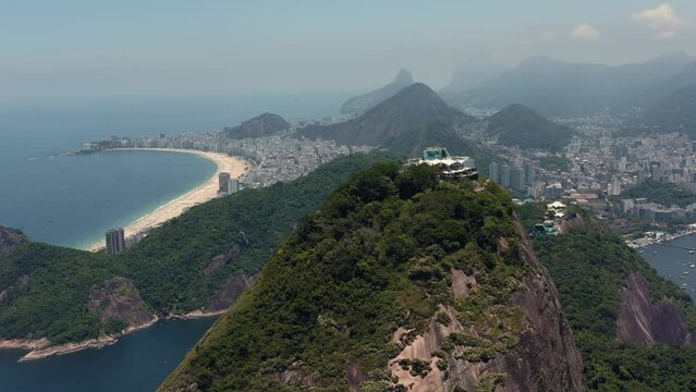 Flying backwards above Sugarloaf Mountain and skyline of Rio de Janeiro and Copacabana Beach as background