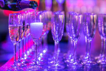 the bartender is pouring glasses of champagne on the background of the restaurant lights from the garlands.
