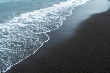 Black volcanic sand on the beach with waves. © SOLDATOOFF