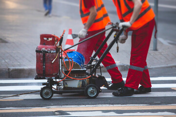 Process of making new road surface markings with a line striping machine, workers improve city infrastructure, demarcation marking of pedestrian crossing with hot melted paint on asphalt pavement