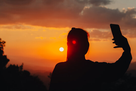 Silhouette of a woman taking a picture in the midst of a beautiful sunset on the mountain.