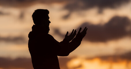 Silhouette of prayer having worship and praying with hands open at sunset 