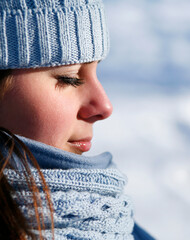 Attractive young woman outdoors in winter wearing blue knit hat and scarf with eyes closed.
