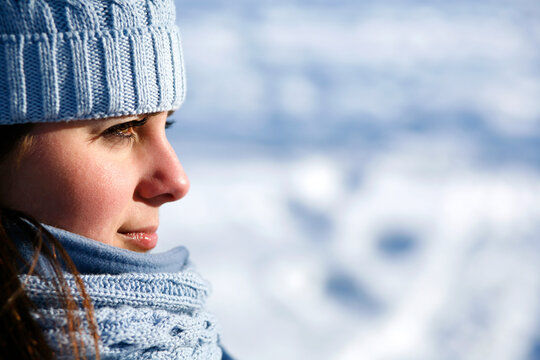 Attractive young woman outdoors in winter wearing blue knit hat and scarf looking forward.