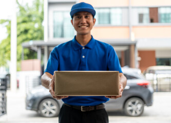 Asian delivery man with parcel in hand of blue uniform sending parcel to customer front of the house from shopping online with good service. Courier man send a package to destination.