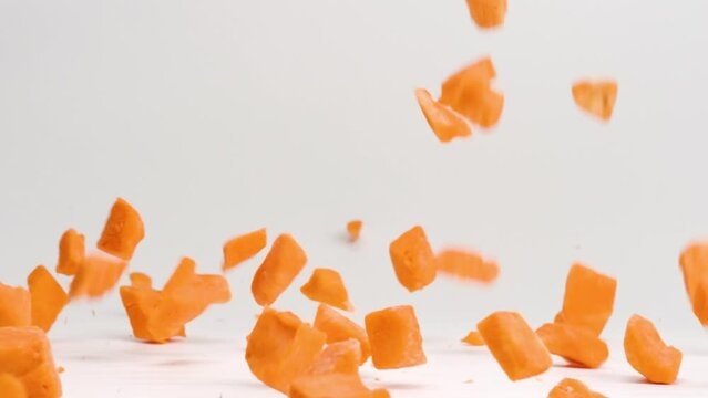 Bright orange cubed sweet potato pieces falling and bouncing onto white table top in slow motion