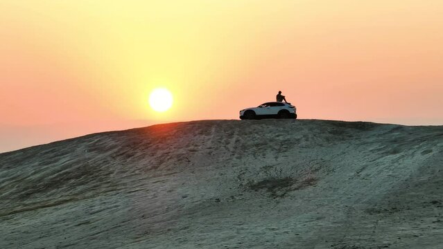 Man sits on a desert hill overlooking a sunrise in ontop of a Mazda car; Israel in the Judean Desert