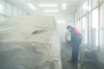 A Worker or Car painter in protective suit and mask paints car bumpers with metallic paint and...
