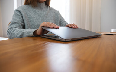 Closeup image of a woman closing or opening a laptop computer on table after finished using it