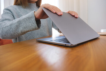 Closeup image of a woman closing or opening a laptop computer on table after finished using it