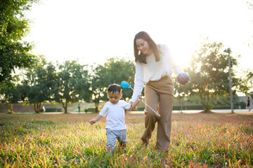 Happy Asian mother and son playing on lawn in the park on a holiday, the family having fun and spending time together, Happy family concept.