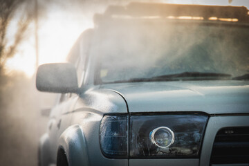 Part of a white car in a cloud of splashing clean water at a self-service car wash.