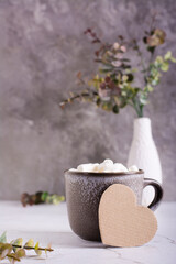 Cardboard heart and a cup of cocoa with marshmallows in a mug on a gray table.  Vertical view