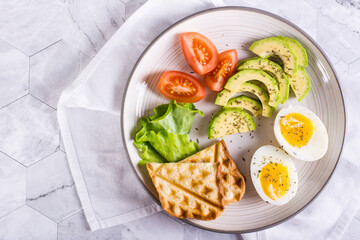 Avocado, soft boiled egg, tomatoes and toast on a plate. Homemade breakfast. Top view. Closeup
