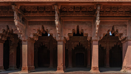 Obraz premium The architecture of the ancient Red Fort. Colonnade with openwork carved arches. Ornaments and patterns on walls and columns. India. Agra.