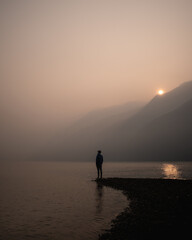 silhouette of a man by a lake during a smokey sunrise