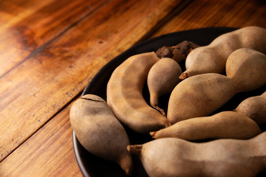 Tamarind fruit (Tamarindus indica) on wooden rustic table. Tropical fruit highly appreciated in several countries of the world. Closeup image.