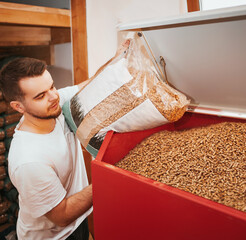 Bearded man puts wood pellet from the bag into the heating boiler oven. Sustainable future concept.
