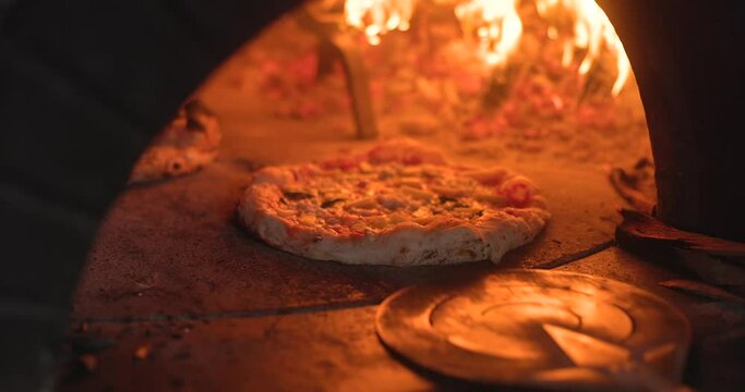 Baking the smoking hot delicious pizza in a traditional Italian oven with wood fire flame. Spin and turn, pull in and pull off in slow motion. 