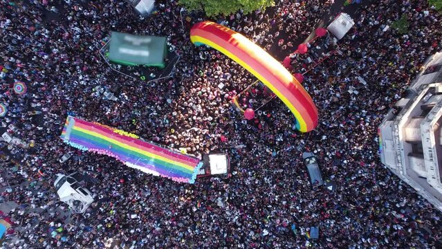 Overhead drone view of Buenos Aires LGBT gay pride parade in Plaza De Mayo square with colored truck and inflatable rainbow. Aerial top down descending