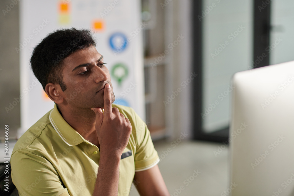 Wall mural portrait of pensive ux designer looking at computer screen deciding what to change in mockup