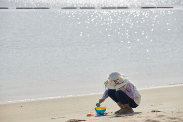 冬の海岸のビーチで砂遊びしている小学生の女の子の様子