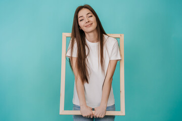 Cute cheerful young woman in white t-shirt and jeans holds frame for Canvas smiling wide stands...