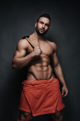 Handsome man in red jumpsuit holding hammer on dark background in studio. Sexy handyman with tool....