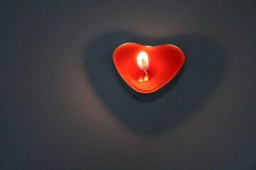 Candle in the shape of a heart burns in the dark