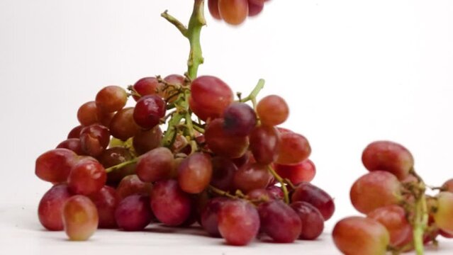 Juicy red grape bunches on the vine falling into a pile on white table top in slow motion