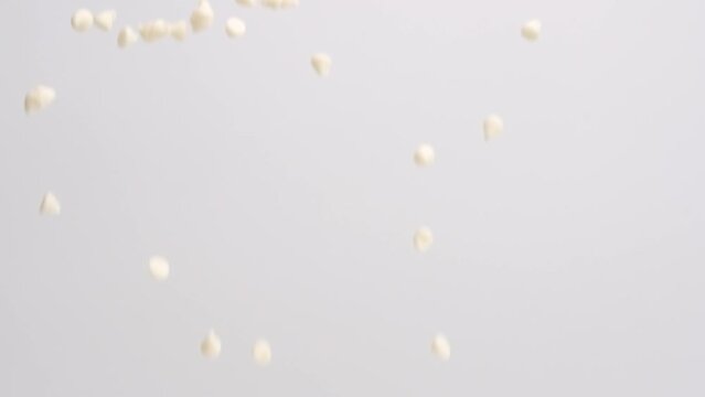 White chocolate chips raining down on white backdrop in slow motion