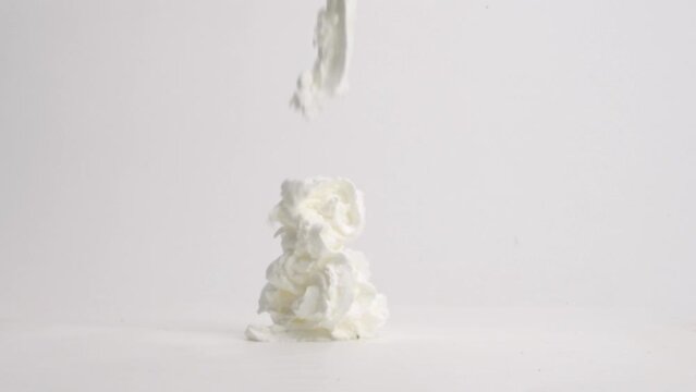 Fresh, fluffy white whipped cream ribbons landing in pile on white table top in slow motion